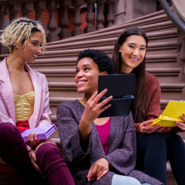 Three women sitting on stairs holding their phones. One woman is showing another her screen.