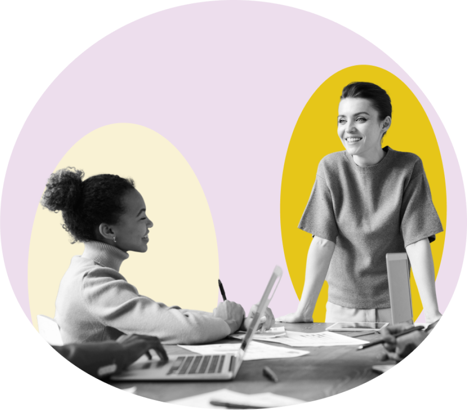 Two women working together at a desk. One is sitting in front of a laptop and the other is standing, smiling. Their image is in black and white and behind them are colourful graphic blocks.